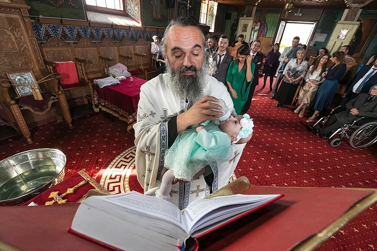 Priest feeds infant while proclaiming Gospel at baptism service